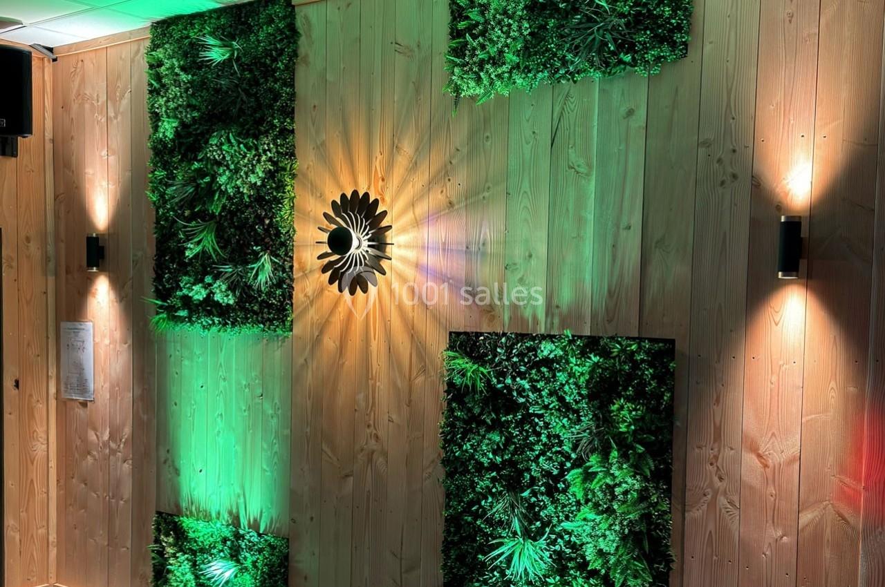 Mur en bois décoré de panneaux végétalisés éclairés par des lumières vertes et une applique murale centrale.