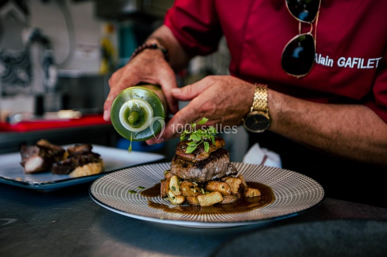 Un chef verse une sauce verte sur un plat de viande et légumes, présenté sur une assiette élégante.