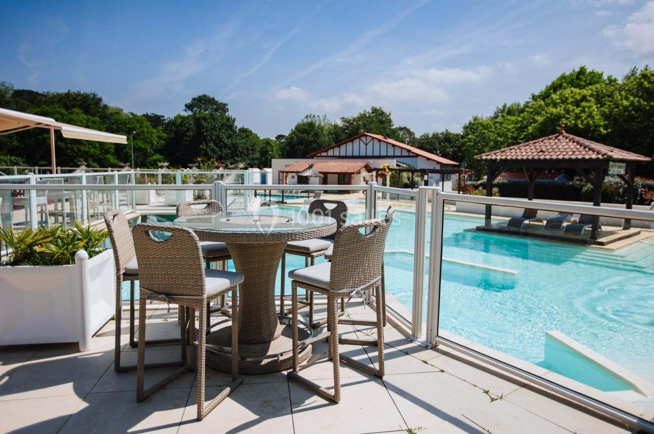 Terrasse avec table et chaises en rotin, donnant sur une piscine extérieure entourée de végétation et d'un pavillon.