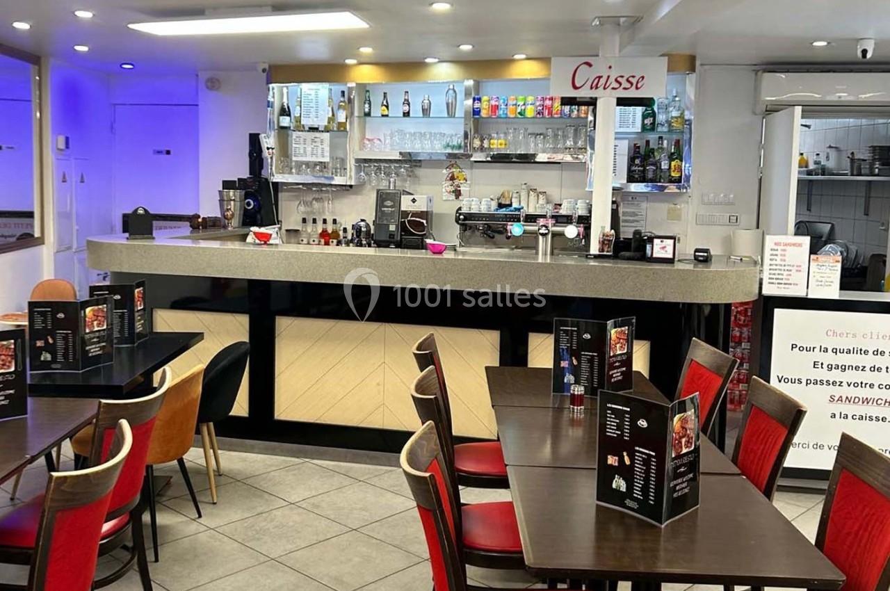 Salle de restaurant avec tables dressées, menus posés et comptoir en arrière-plan équipé de machines et étagères.