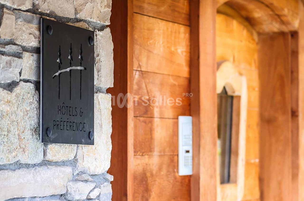 Plaque en métal avec un logo et l'inscription ’Hôtels & Préférence’, fixée sur un mur en pierre près d'une porte en bois.