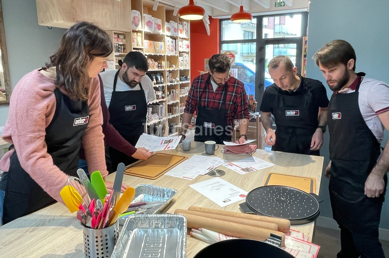 Des personnes en tablier participent à un atelier culinaire, entourées d'ustensiles de cuisine sur une table.