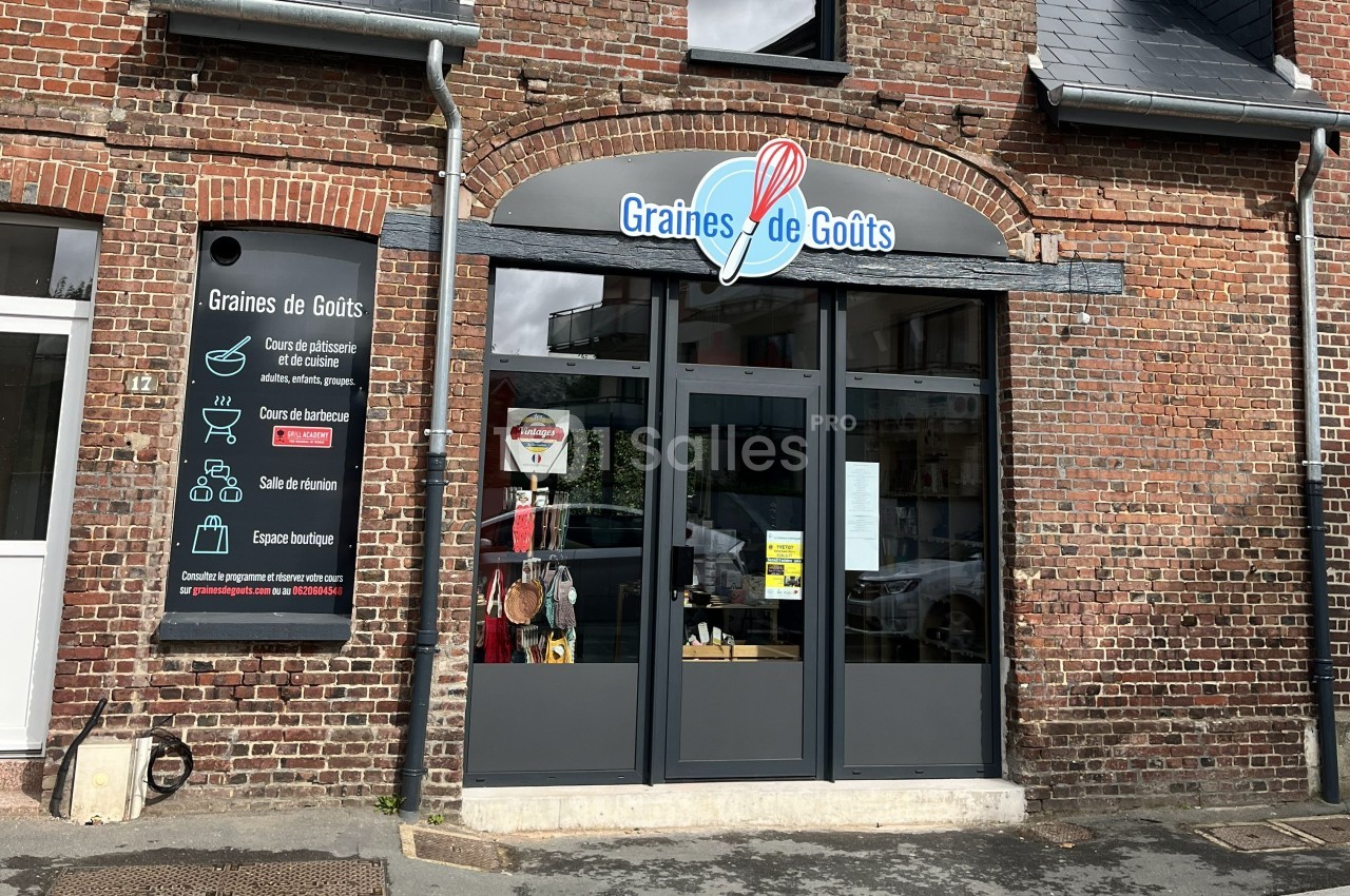 Façade en briques d'un commerce nommé ’Graines de Goûts’ avec une vitrine et un panneau d'informations à gauche.
