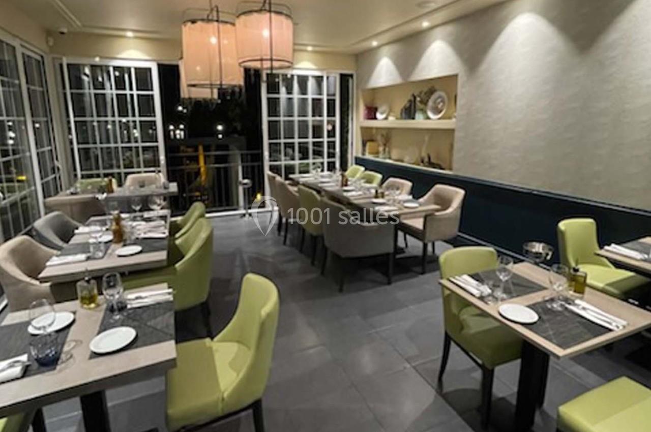 Salle de restaurant moderne avec tables dressées, chaises colorées et grandes baies vitrées donnant sur l'extérieur.