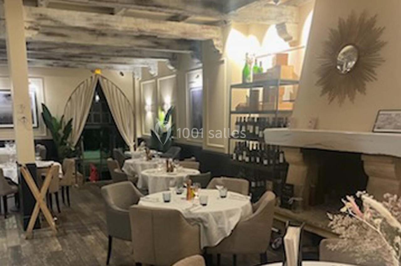 Salle de restaurant élégante avec tables dressées, chaises rembourrées, cheminée et éclairage chaleureux.
