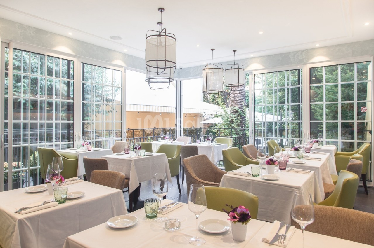 Salle de restaurant lumineuse avec grandes baies vitrées, tables dressées et chaises modernes dans un cadre élégant.
