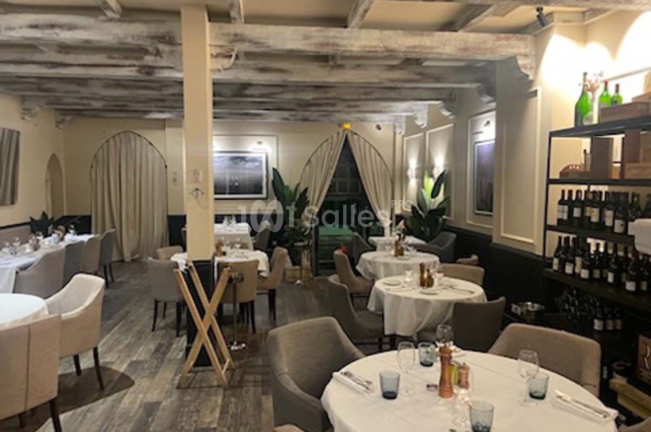 Salle de restaurant élégante avec tables dressées, chaises confortables, étagères à vin et éclairage chaleureux.