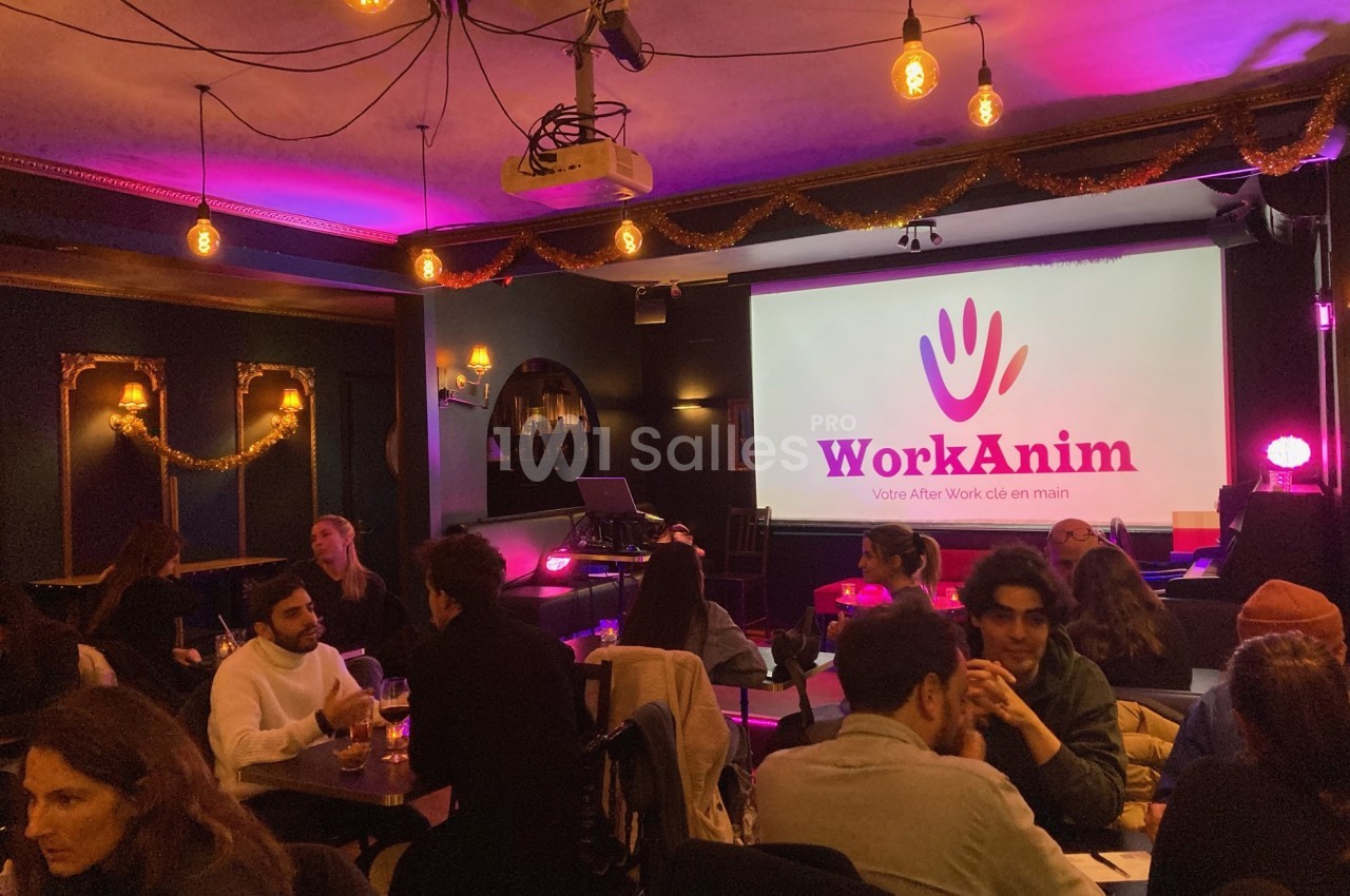 Salle animée avec des personnes assises à des tables, éclairage tamisé et écran affichant ’WorkAnim’.
