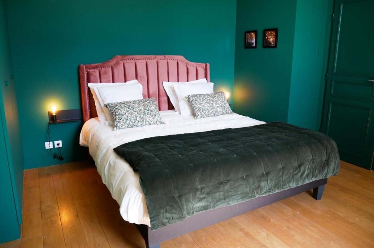 Lit double avec tête de lit rose, draps blancs et plaid vert foncé, dans une chambre aux murs verts.