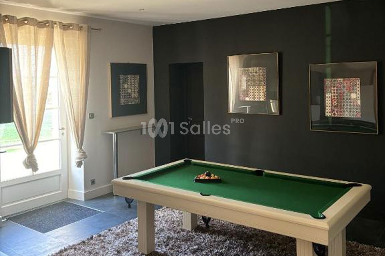 Table de billard blanche avec tapis vert dans une pièce lumineuse, décorée de tableaux et de rideaux beiges.