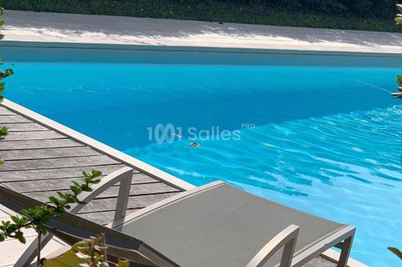 Transat gris sur une terrasse en bois près d'une piscine entourée de végétation.