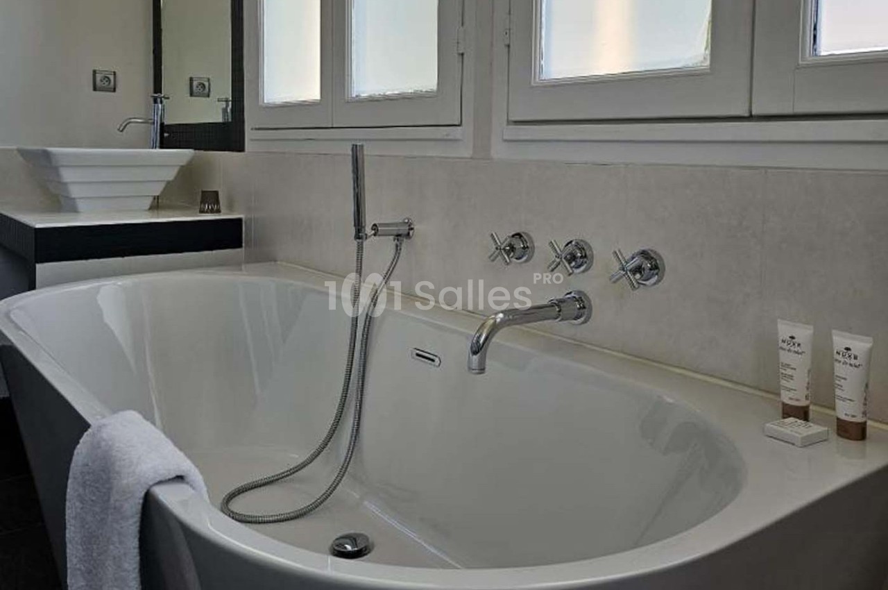 Baignoire blanche avec robinetterie moderne, serviette accrochée et produits de soin posés sur le rebord.