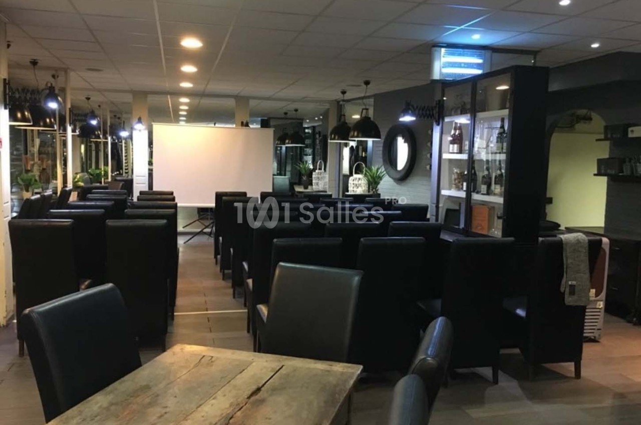 Salle aménagée avec des fauteuils noirs disposés face à un écran de projection, éclairée par des lumières suspendues.