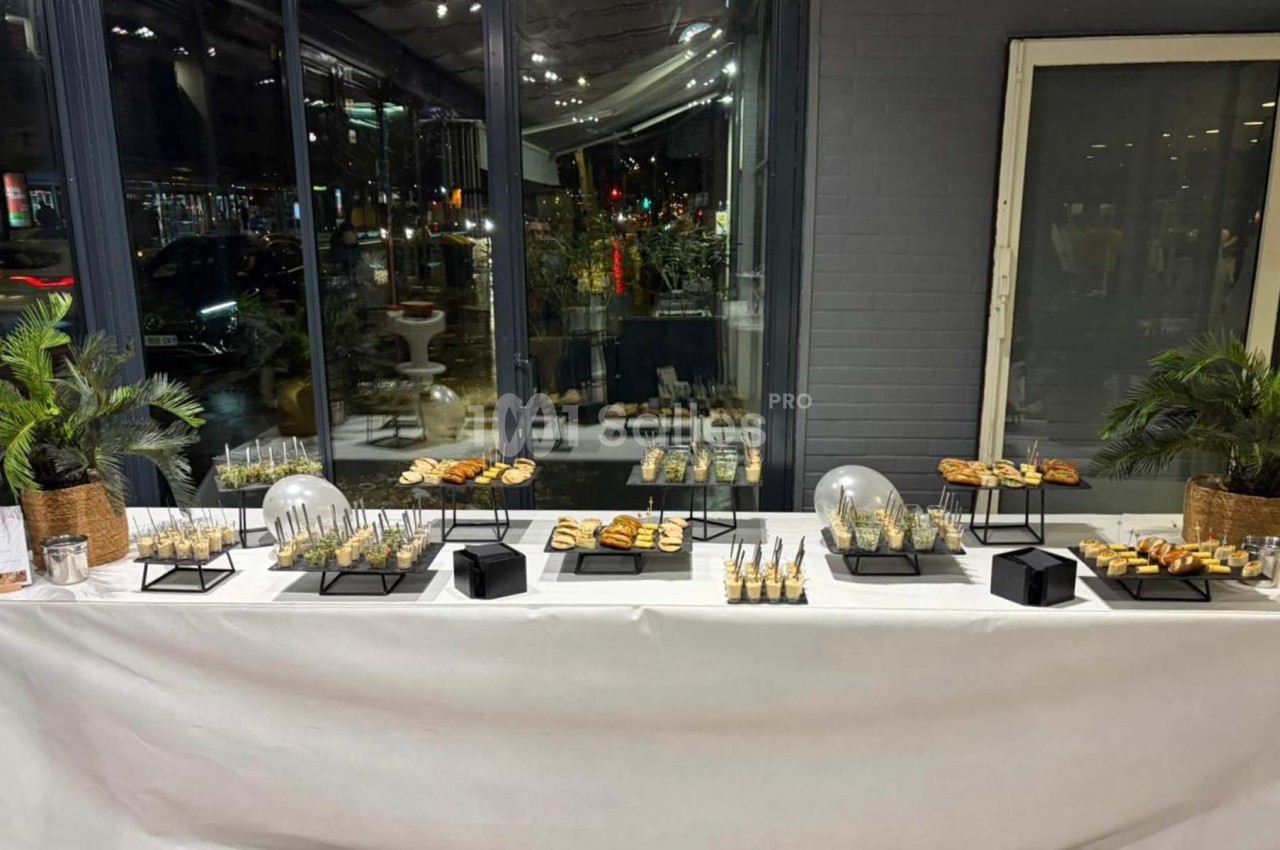 Buffet de réception avec verrines, amuse-bouches et décorations végétales, installé devant une grande baie vitrée.
