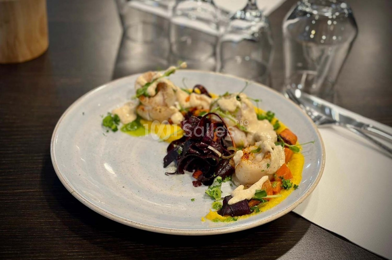 Assiette de noix de Saint-Jacques accompagnées de légumes colorés et d'une sauce, servie sur une table sombre.