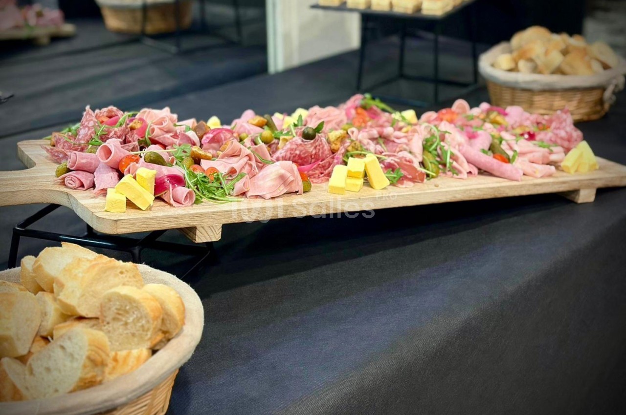 Plateau de charcuterie variée avec fromages, salade et pain tranché disposés dans des paniers en osier.