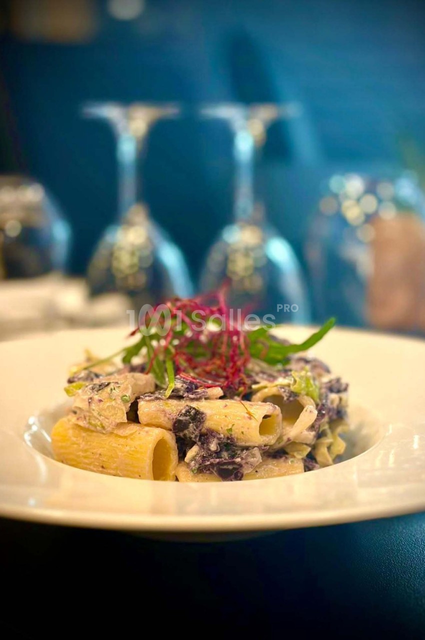 Assiette de pâtes rigatoni garnies de sauce crémeuse, légumes et herbes, servie sur une table élégamment dressée.