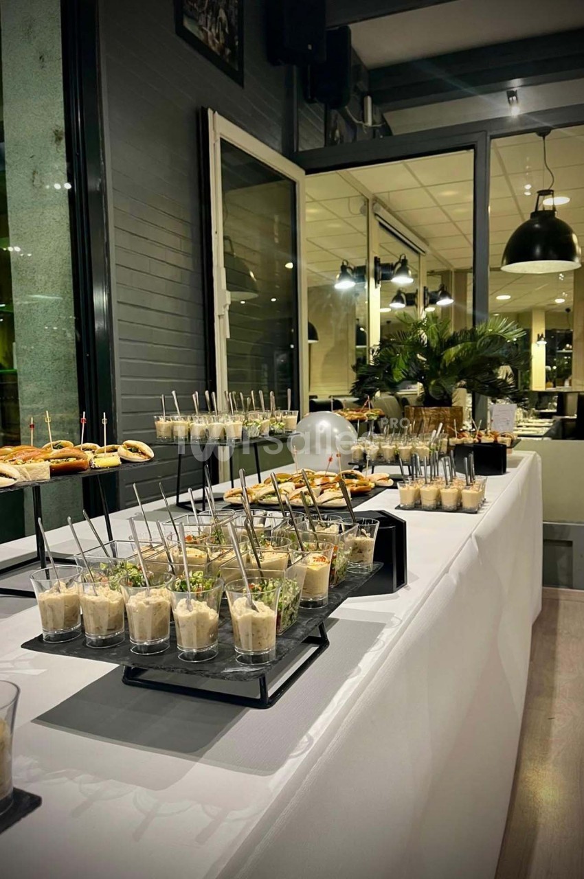 Buffet élégant avec verrines, amuse-bouches et petits sandwichs disposés sur une table blanche dans un cadre moderne.
