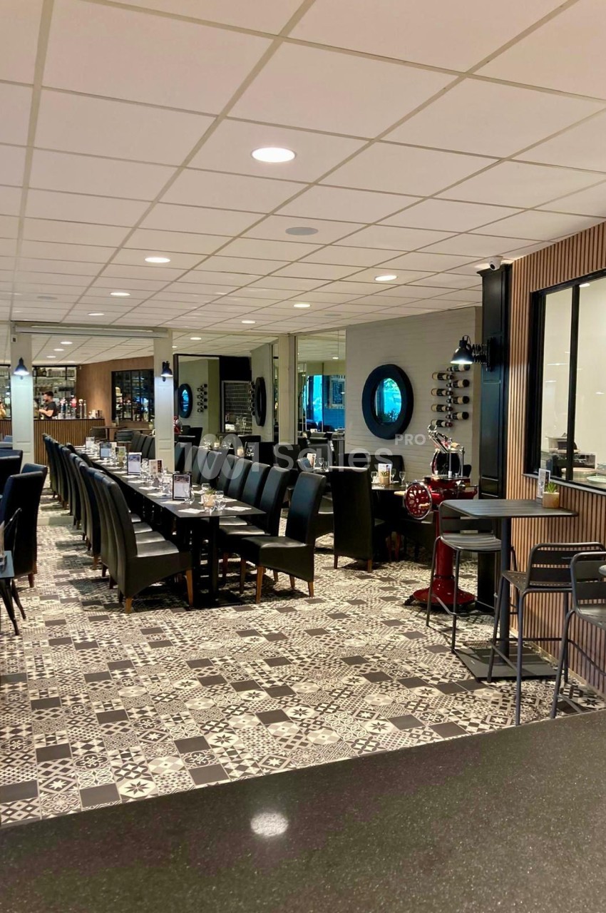Salle de restaurant moderne avec tables alignées, chaises noires et sol en carreaux à motifs géométriques.