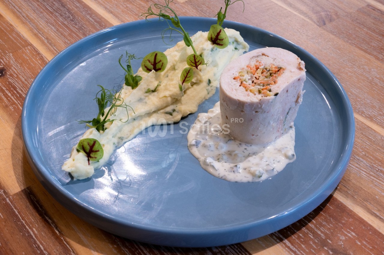 Roulé de volaille farci, purée décorée de pousses et sauce blanche, présenté sur une assiette bleue.