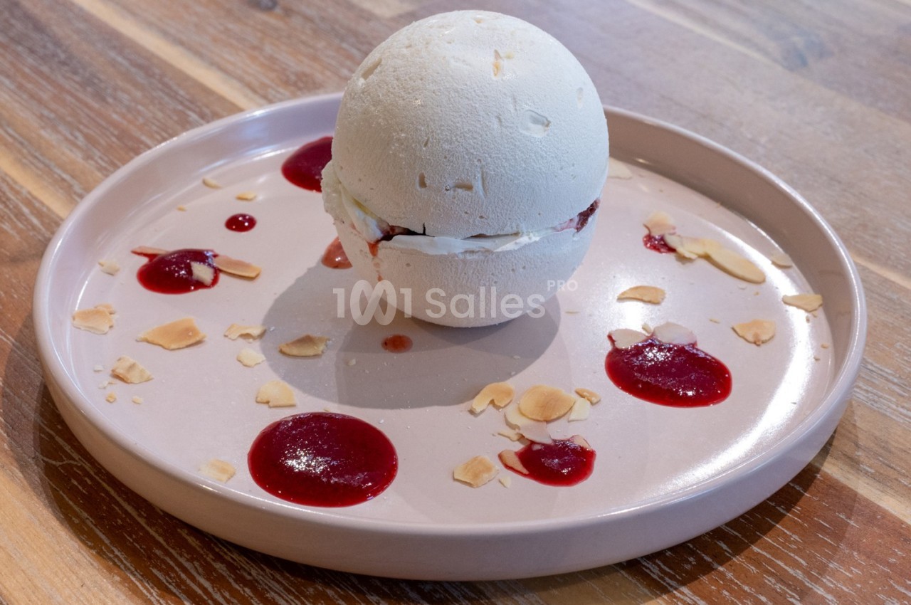 Dessert sphérique en meringue garni de crème et fruits rouges, présenté sur une assiette avec coulis et éclats d'amandes.