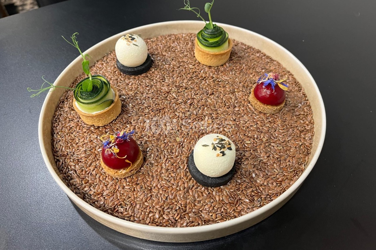 Assiette de présentation gastronomique avec lit de grains et petits desserts décorés aux fleurs.