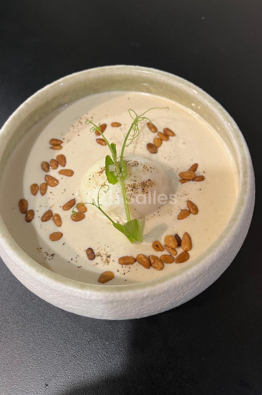 Soupe crémeuse beige en bol blanc, garnie d'amandes grillées et d'une brindille de microgreen.