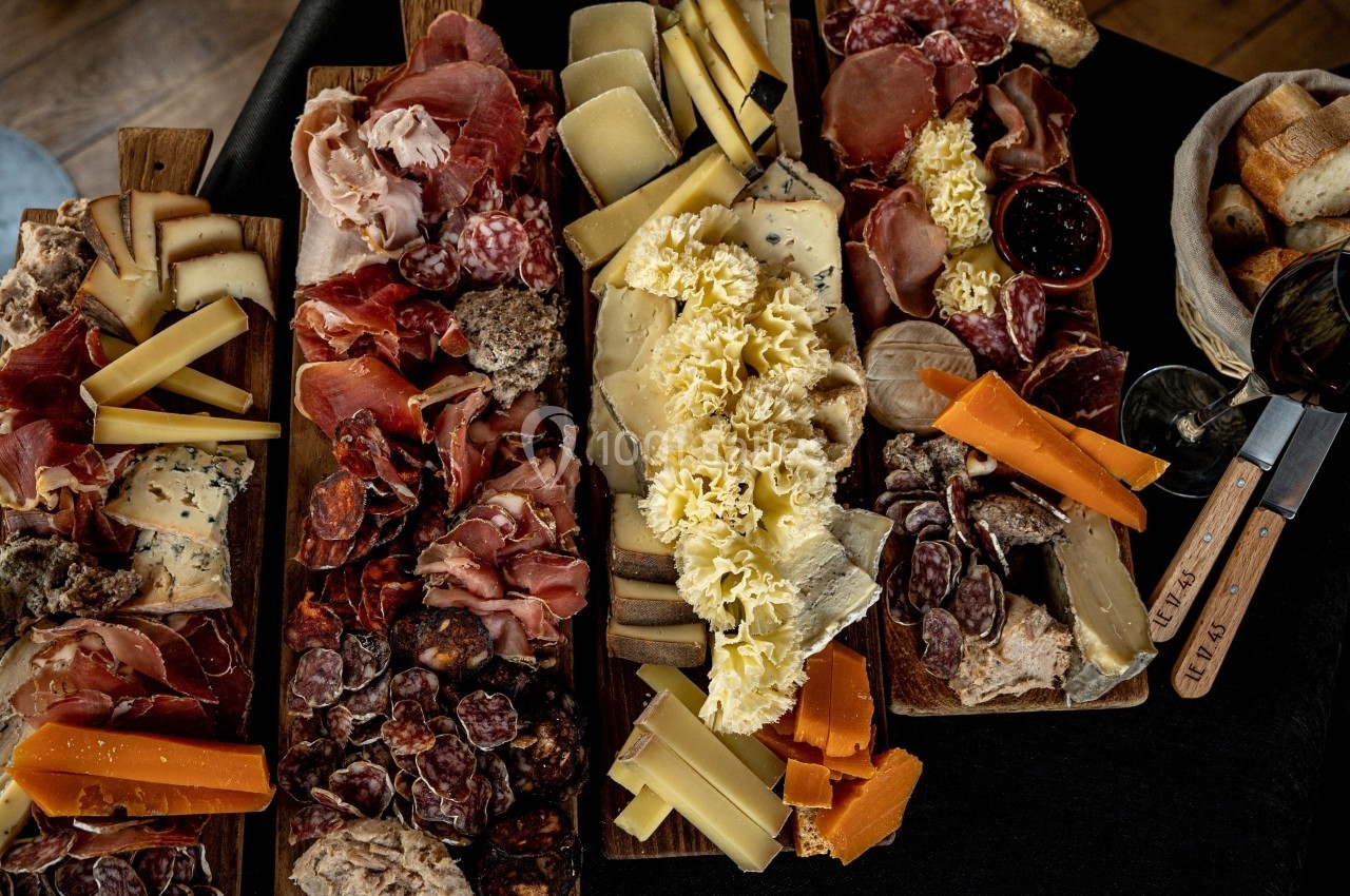 Plateaux de charcuteries et fromages variés disposés sur des planches en bois, accompagnés de pain et d'un verre de vin.