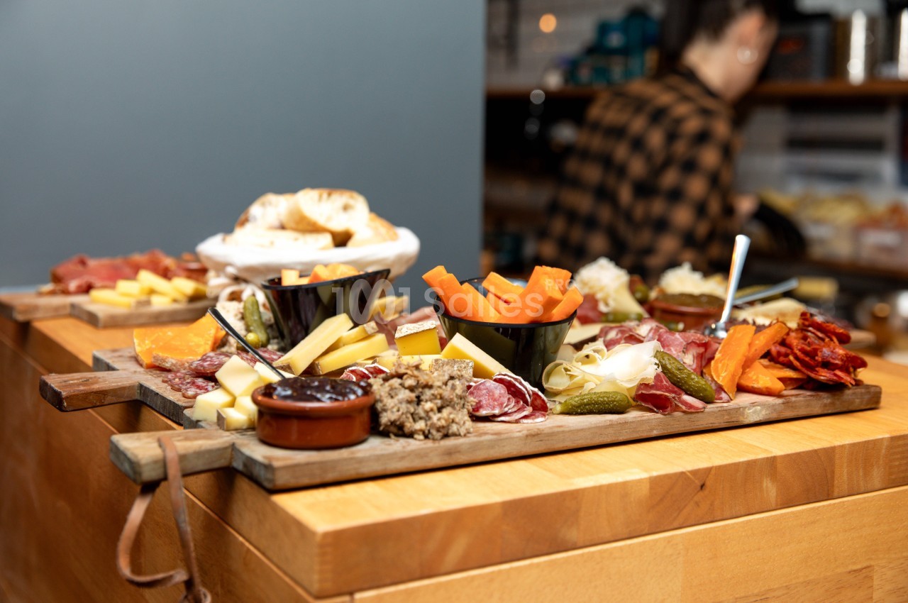 Plateau de charcuterie et fromages variés avec légumes, cornichons et sauces, présenté sur une table en bois.
