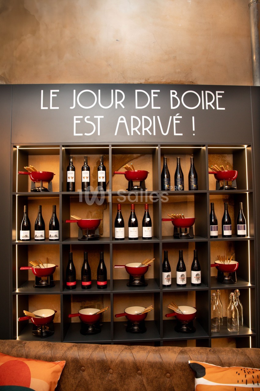 Étagère murale avec bouteilles de vin, caquelons rouges et baguettes, sous une inscription humoristique.
