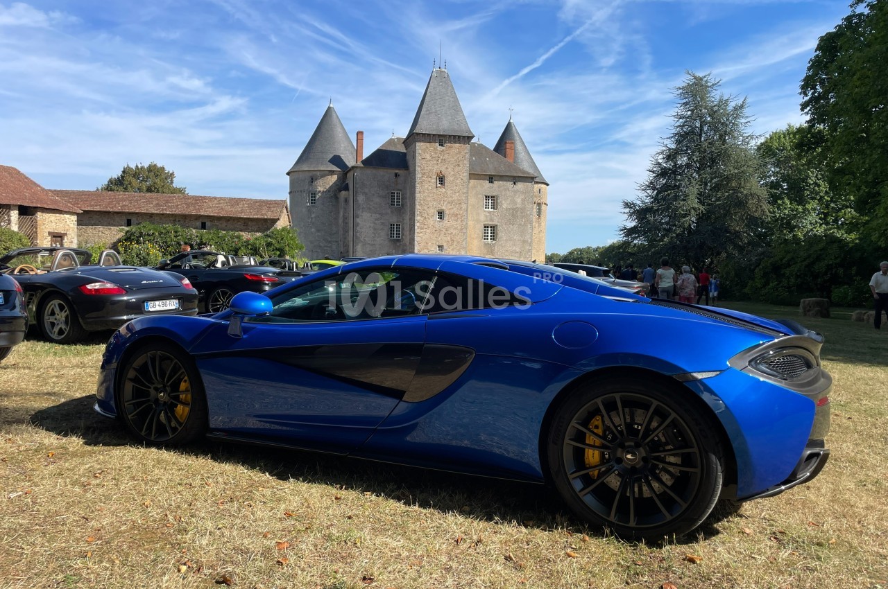 Voiture de sport bleue stationnée sur une pelouse devant un château ancien sous un ciel dégagé.