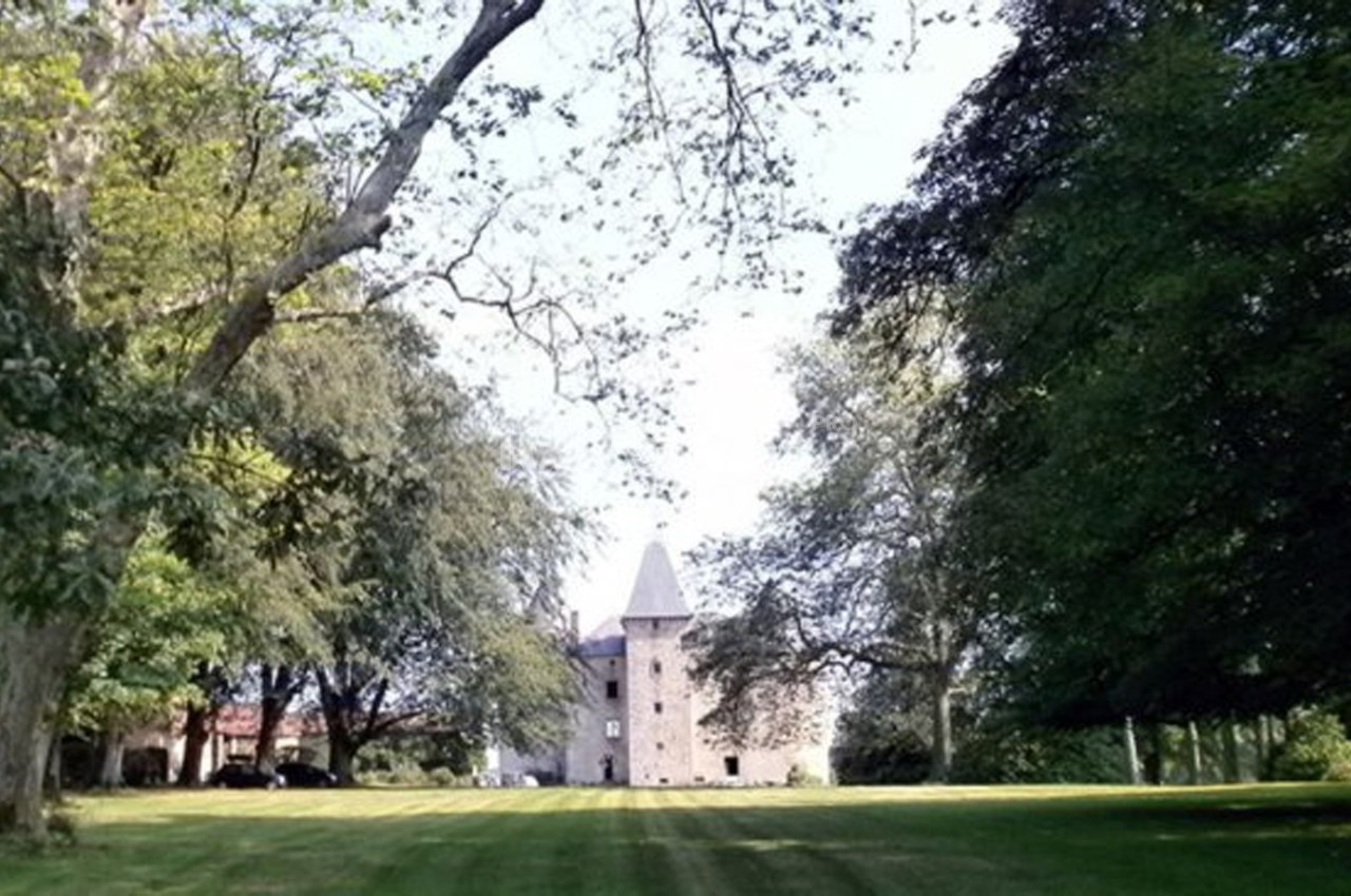 Vue d'un château en pierre entouré d'arbres et d'une pelouse bien entretenue sous un ciel dégagé.