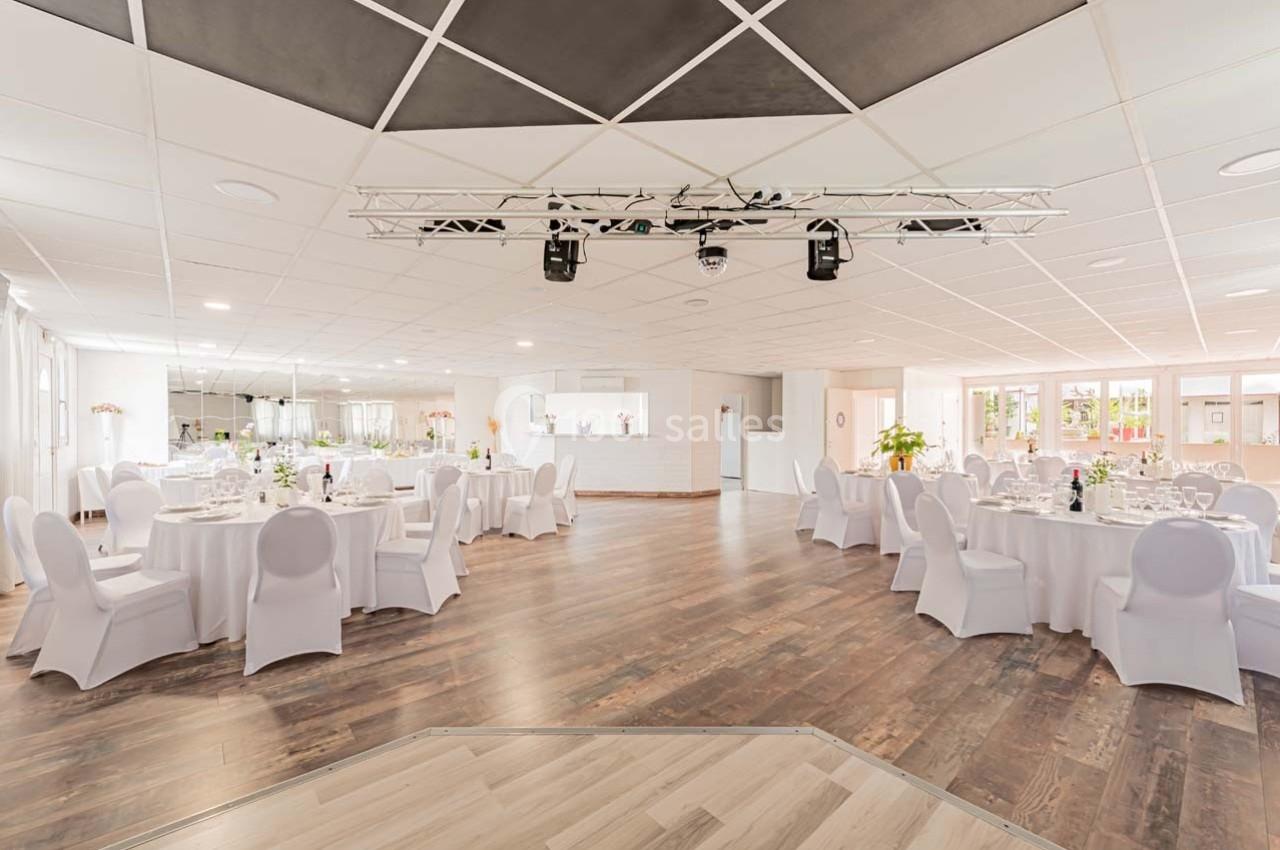 Salle de réception lumineuse avec tables rondes dressées, chaises blanches et parquet en bois clair.