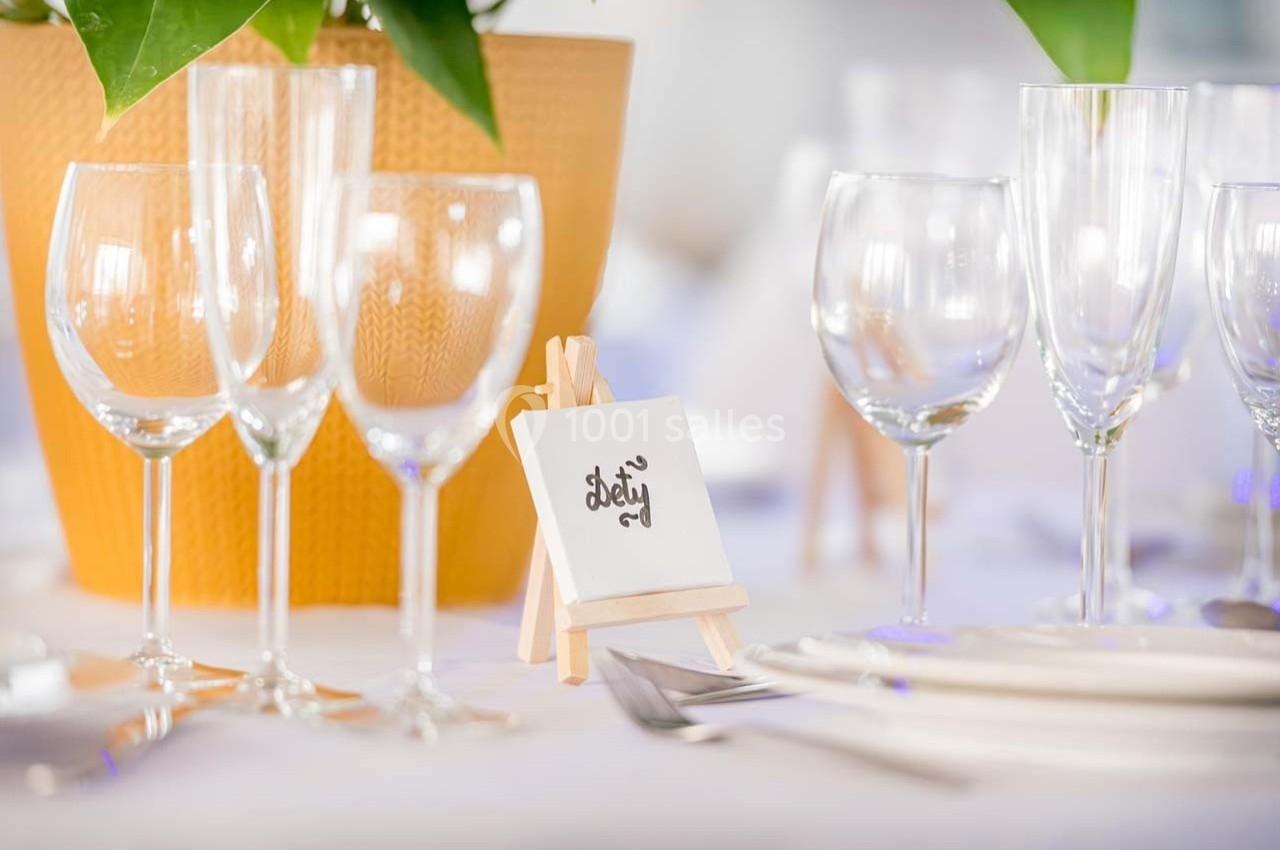 Verres à pied et assiettes disposés sur une table dressée, avec un chevalet portant une carte décorative.