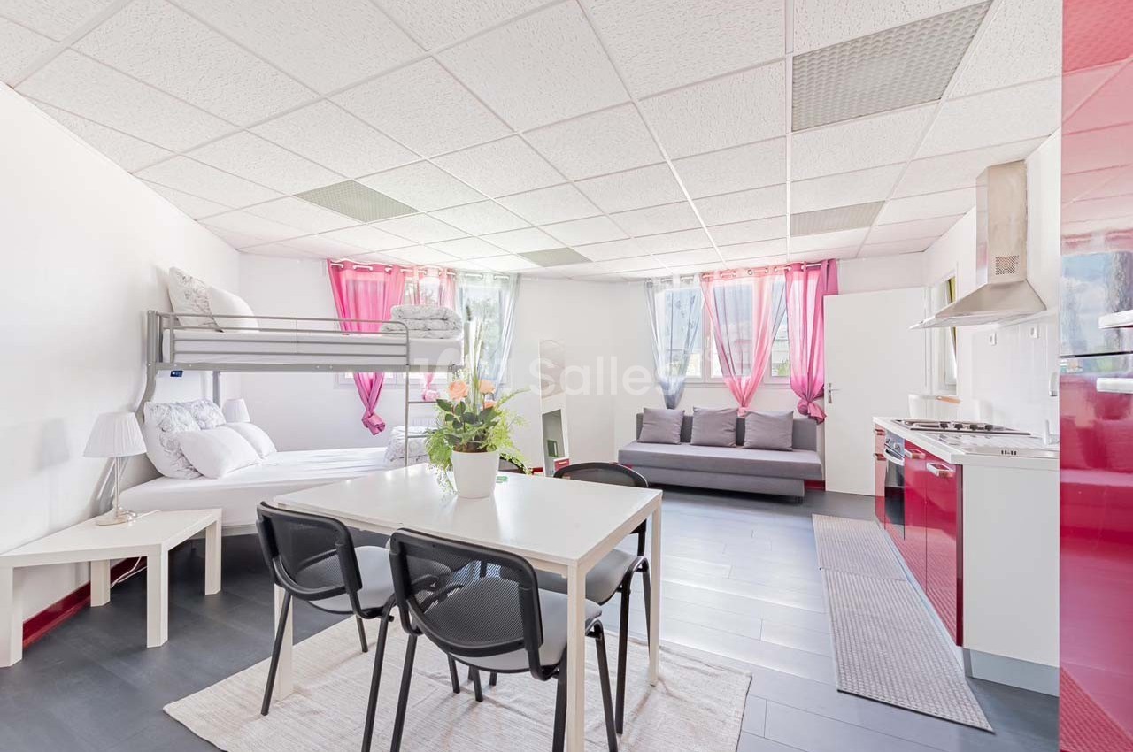 Studio lumineux avec lit superposé, canapé, table à manger, cuisine équipée et décoration minimaliste.