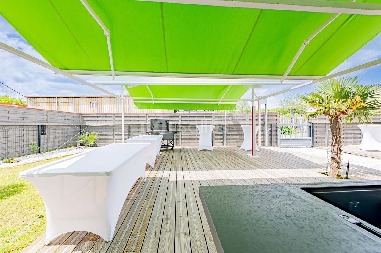 Terrasse en bois avec des tables habillées de nappes blanches, abritée par des toiles tendues vertes.