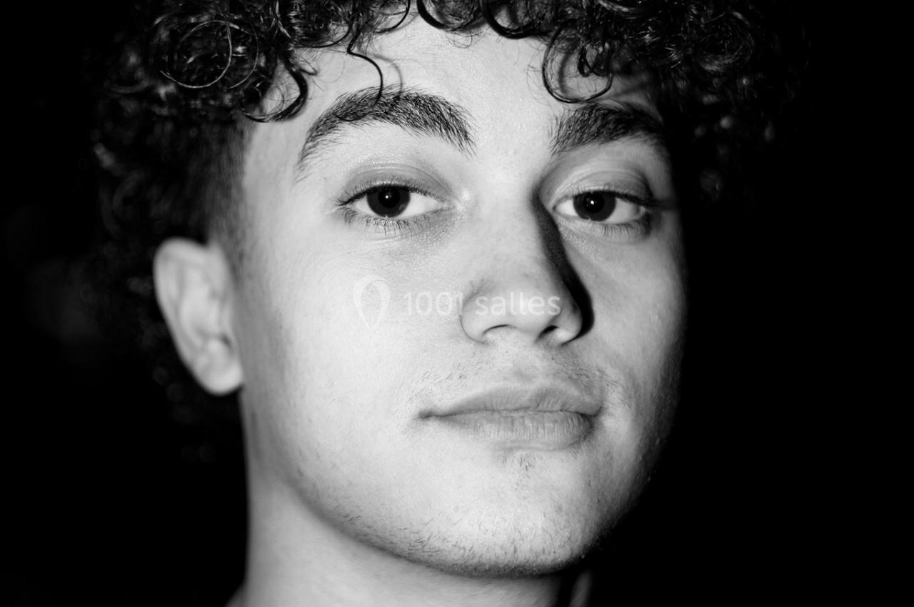 Jeune homme aux cheveux bouclés regardant l'objectif, éclairé par une lumière contrastée en noir et blanc.