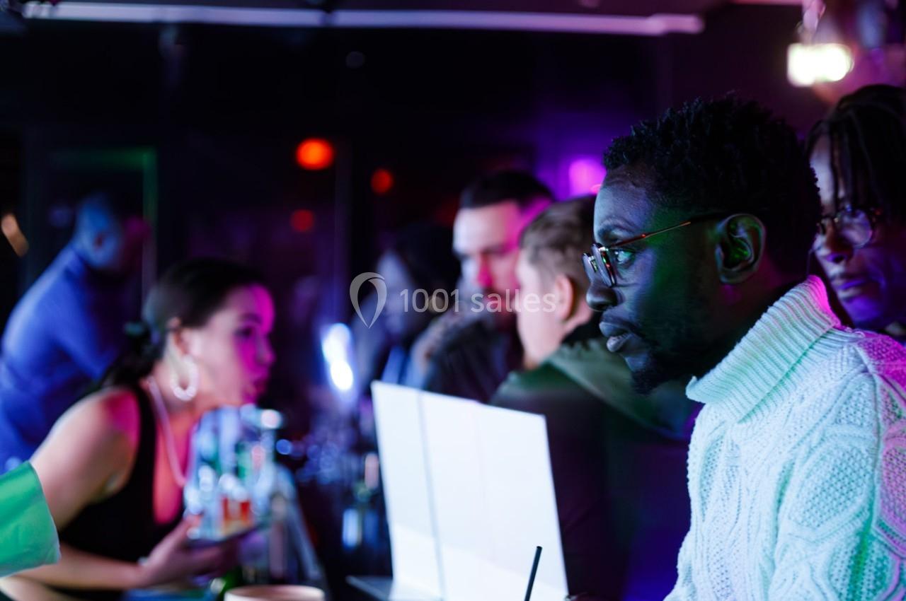 Des personnes discutent et boivent au comptoir d'un bar éclairé par des lumières colorées.