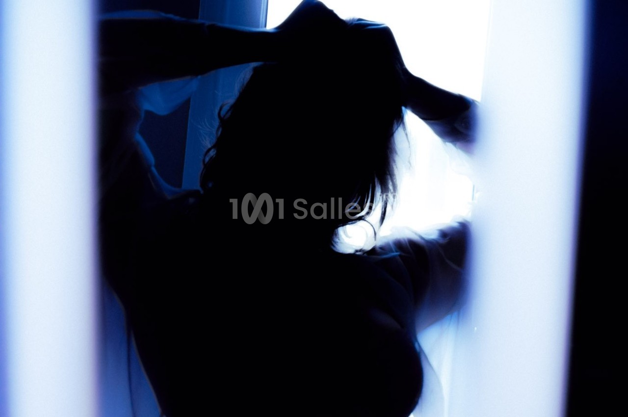Silhouette d'une personne de dos, les mains dans les cheveux, éclairée par une lumière vive en arrière-plan.