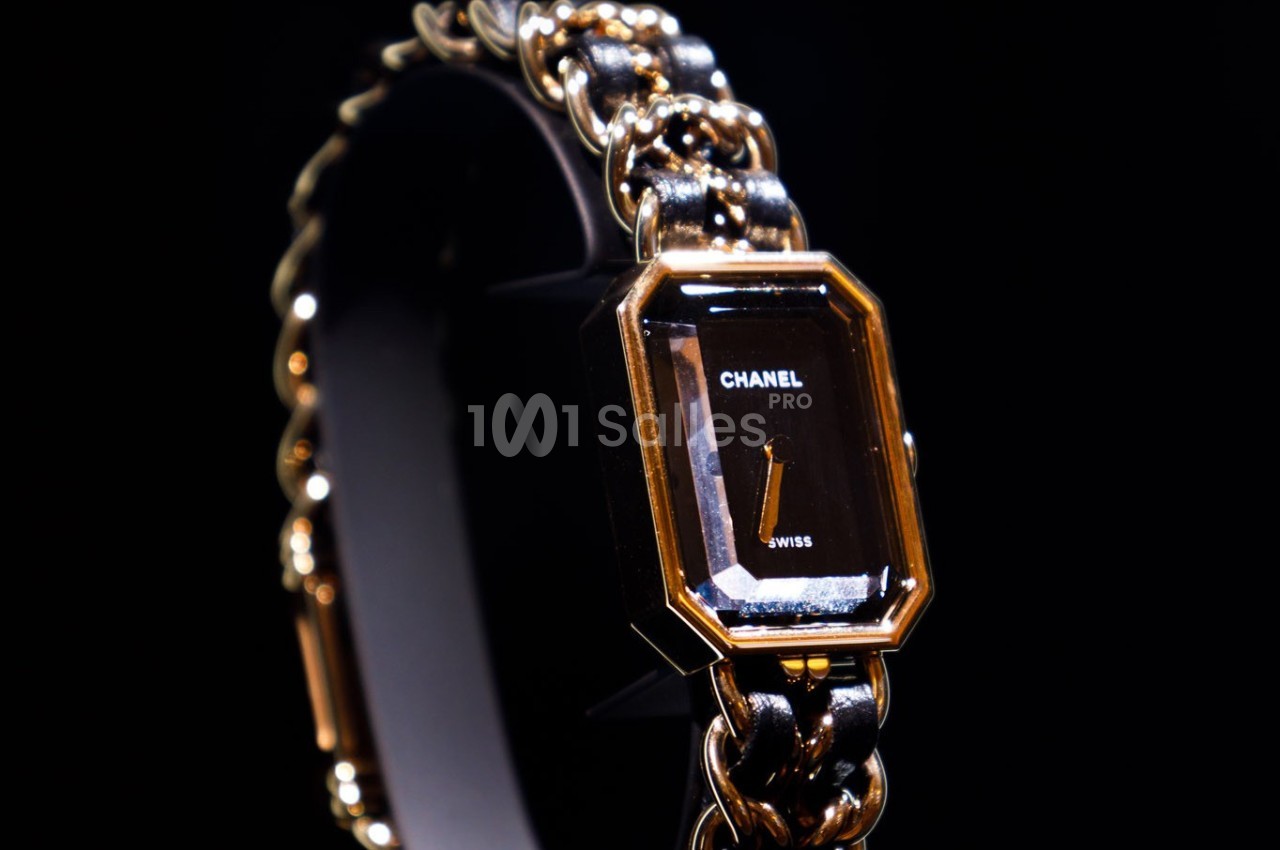 Montre élégante avec cadran noir rectangulaire, boîtier doré et bracelet en chaîne métallique entrelacée.