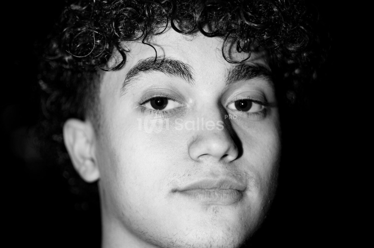 Portrait en noir et blanc d'un jeune homme aux cheveux bouclés, regardant directement vers l'objectif.