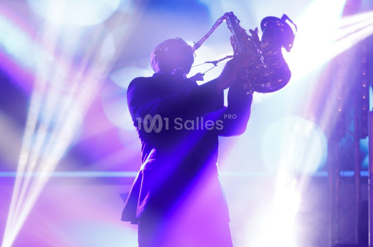 Un musicien joue du saxophone sous des lumières colorées dans une ambiance de concert.