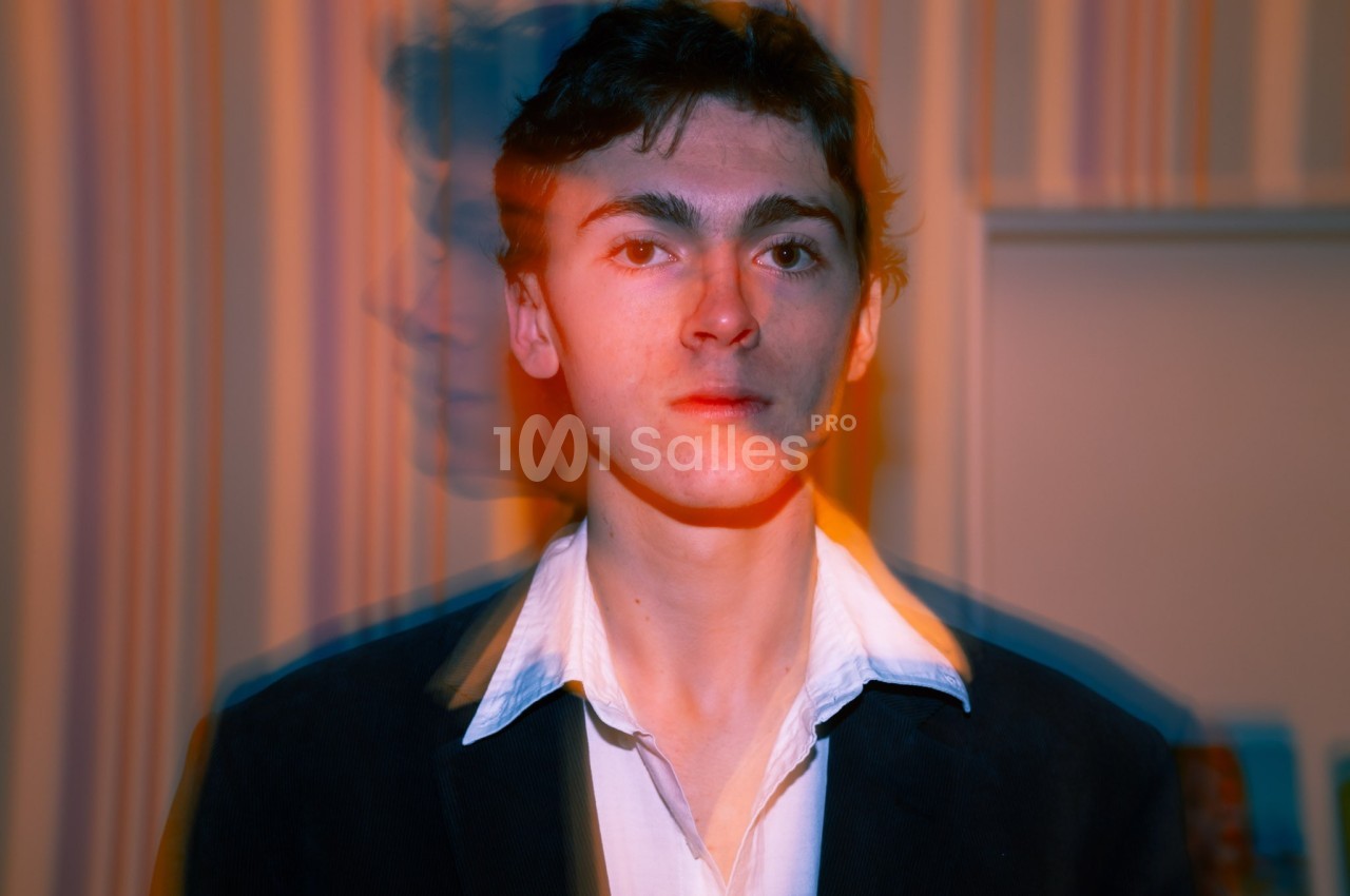 Portrait d'un homme en veste sombre et chemise blanche, avec un effet de flou et de dédoublement coloré en arrière-plan.