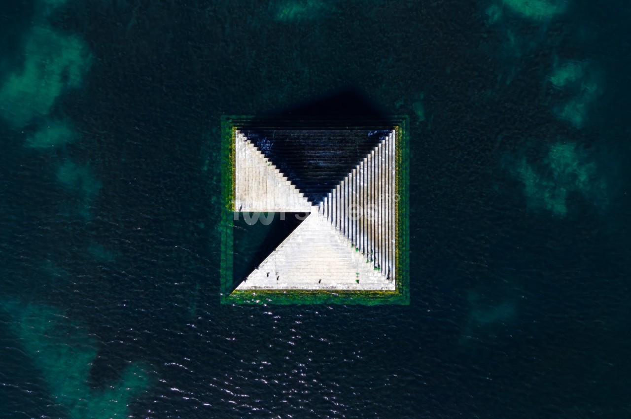 Vue aérienne d'une structure géométrique flottante sur une étendue d'eau sombre avec des reflets et des nuances.