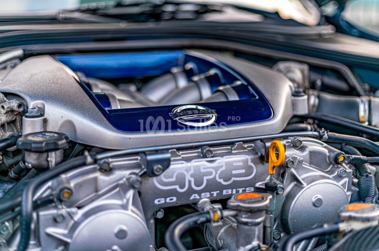 Moteur de voiture avec logo Nissan visible, entouré de composants mécaniques et détails métalliques.