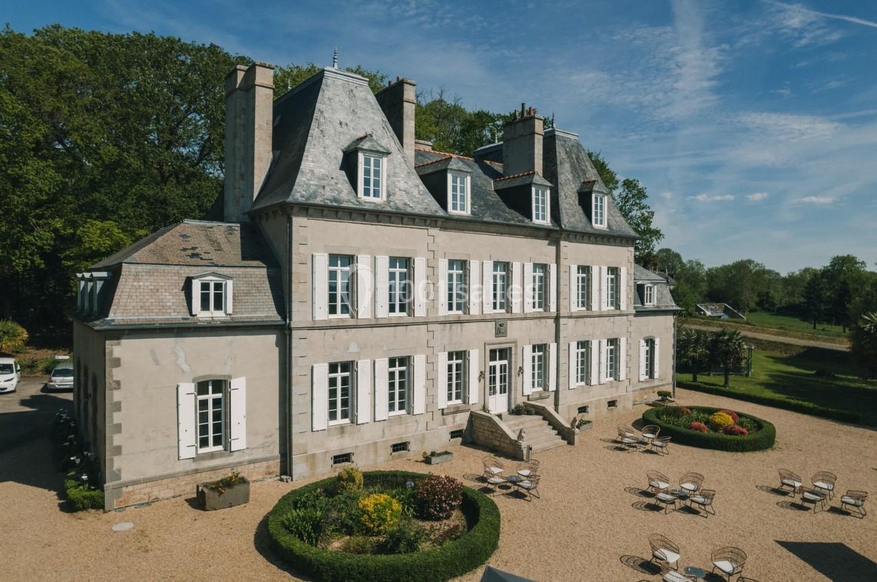 Façade d'un manoir en pierre avec toit en ardoise, entouré de jardins et de mobilier d'extérieur sur une cour gravillonnée.