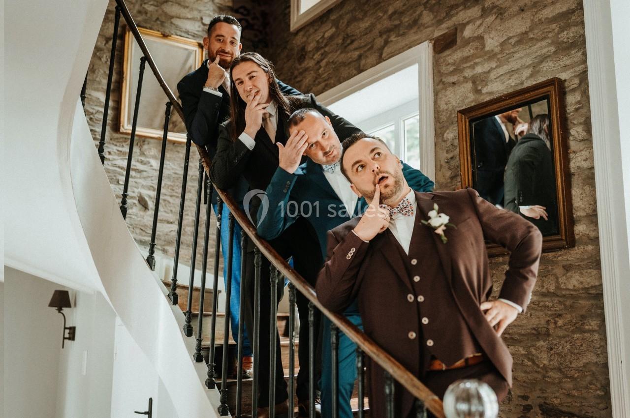 Quatre hommes en costume posent de manière humoristique sur un escalier intérieur en pierre.