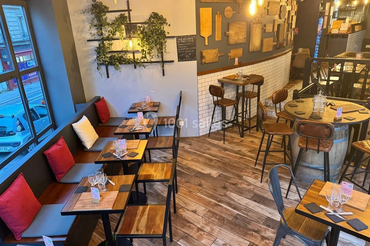 Salle de restaurant lumineuse avec tables en bois, chaises variées, décor mural et plantes suspendues.