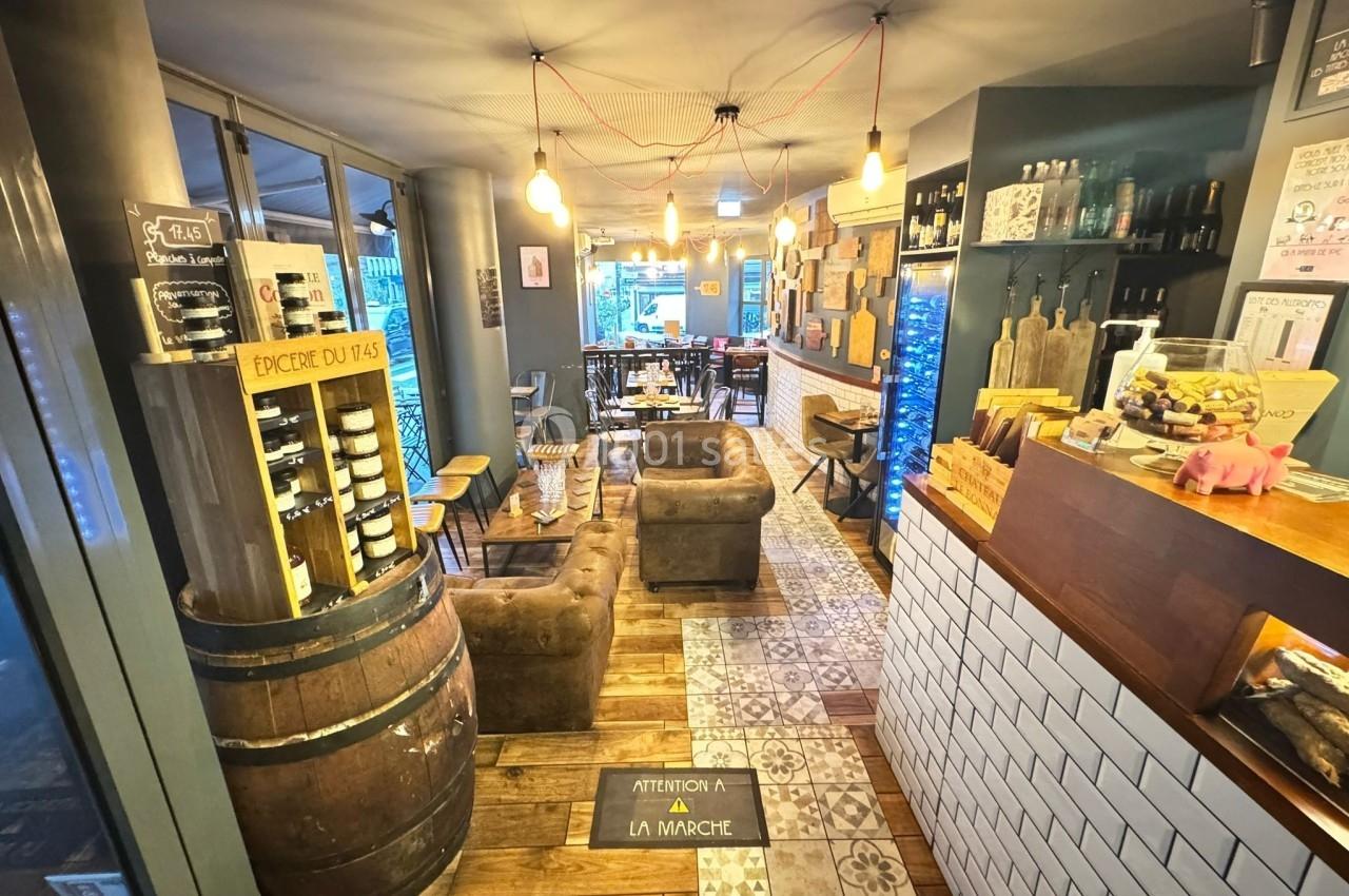 Intérieur chaleureux d'un café avec fauteuils, bar en bois, étagères de produits et éclairage tamisé.