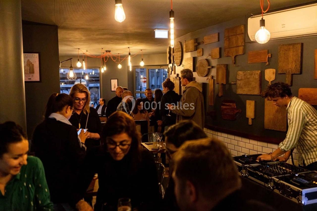 Des personnes discutent et se détendent dans un bar chaleureux, avec un DJ jouant de la musique en arrière-plan.
